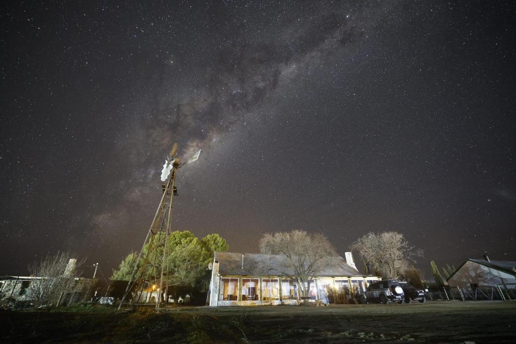 eine sternenklare Nacht mit einem Haus mit einer Windmühle in der Unterkunft Van Wyks Hartshuis in Sutherland