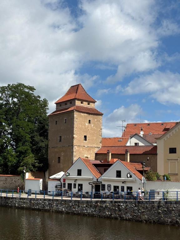 a building with a tower next to a river at Apartmán Železná panna in České Budějovice