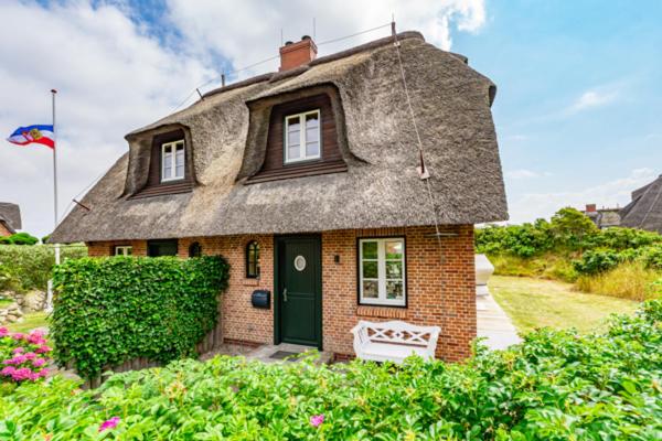 a house with a thatched roof with a bench in front at Haus Düne in List