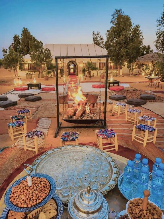 a fire pit with tables and chairs and a fireplace at Merzouga Retreat Camp in Merzouga