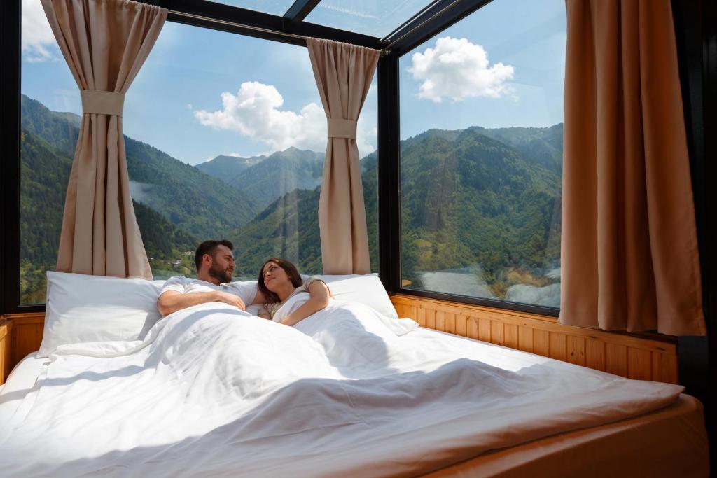 a bride and groom laying in bed in front of a window at Sky Glass Cottage in Kʼveda Chʼkhutunetʼi