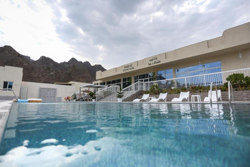 a swimming pool with chairs in front of a building at paradise resort and spa in Hatta