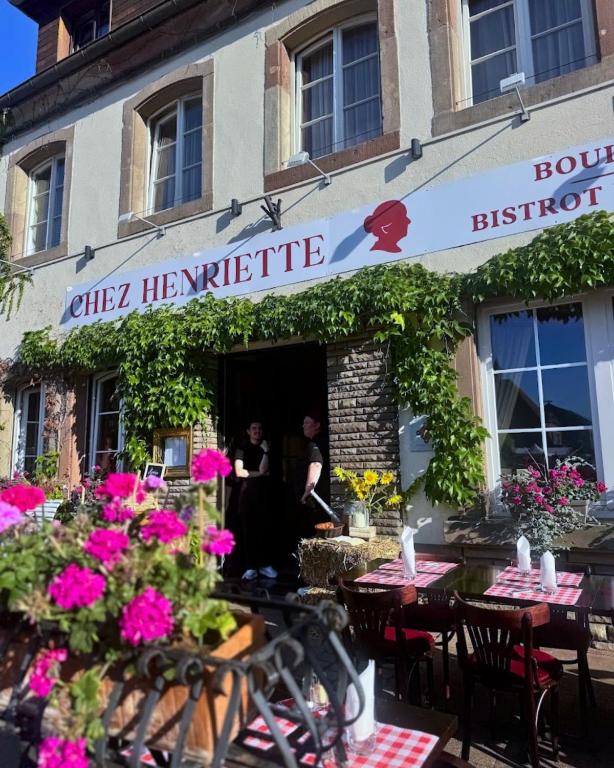a couple in the doorway of a restaurant with tables and flowers at Hôtel Restaurant Chez Henriette in Phalsbourg