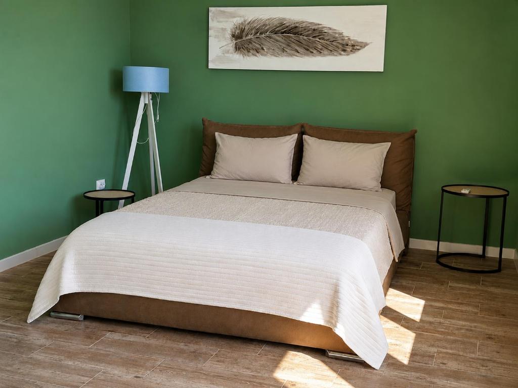 a bed in a green bedroom with two tables at CERES APARTMENTS free parking, kitchen & wi-fi in Utjeha