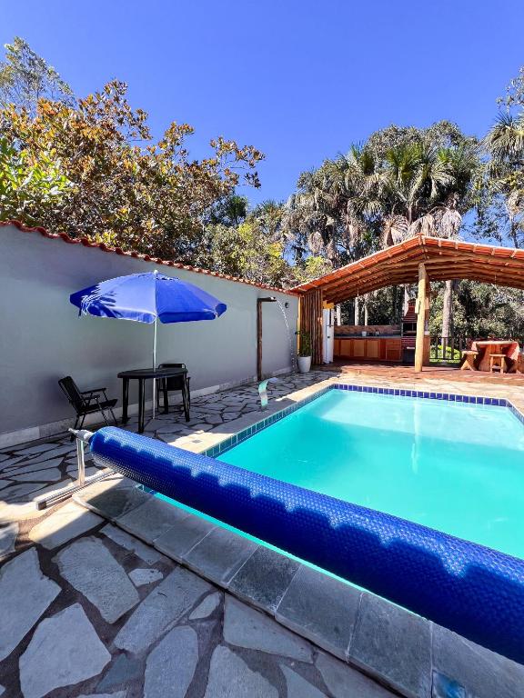 a blue swimming pool with an umbrella and a table and an umbrella at Chácara buriti in Pirenópolis