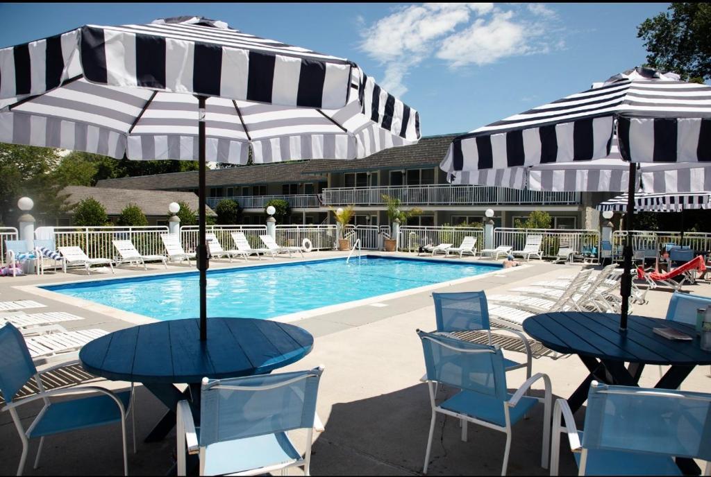 two tables with umbrellas and chairs next to a pool at Cape Harbor Motor Inn in Cape May