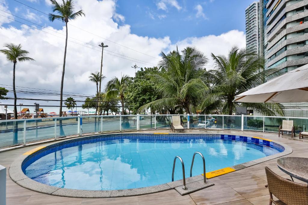 a large swimming pool with palm trees and a building at Hotel Beira Mar Boa Viagem By Flatbpaiva in Recife