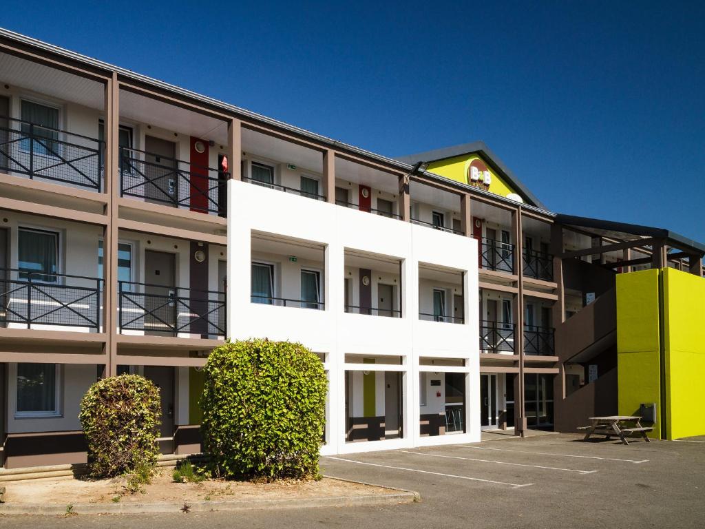 un grand bâtiment blanc avec un parking dans l'établissement B&B HOTEL Saint-Brieuc, à Trégueux