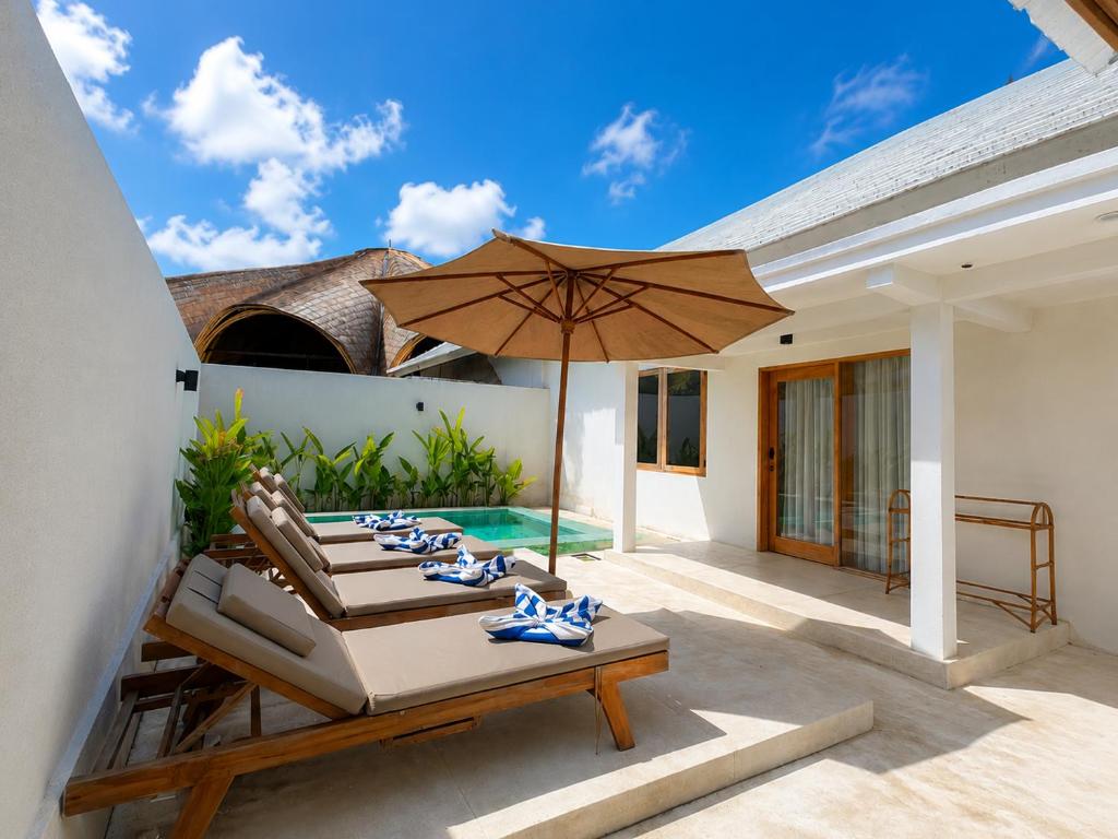 a patio with an umbrella and chairs and a pool at Villa Marieta - Two Bedrooms Private Villa in Kuta Lombok