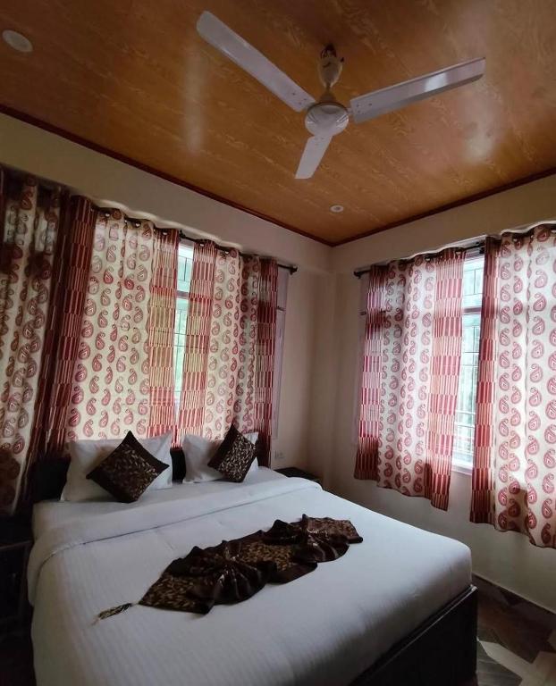 a bedroom with a bed with a ceiling fan and windows at THE PINE STAy in Chail