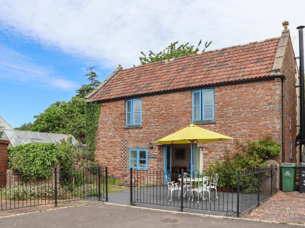 a brick house with a yellow umbrella and chairs at The Quarry Stables in Cheddar