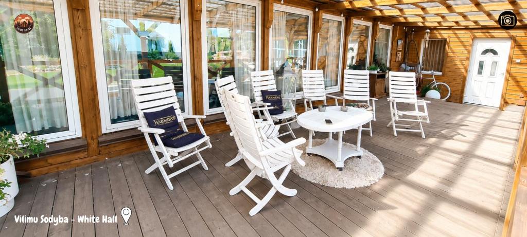 a patio with white chairs and a table on a porch at Vilimu Sodyba - White Hall in Kriukai