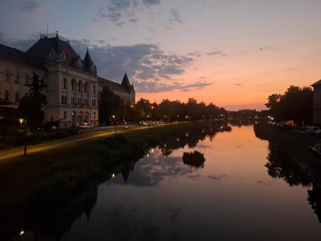 a river in front of a building at sunset at Apartman Lola Ruža in Zrenjanin