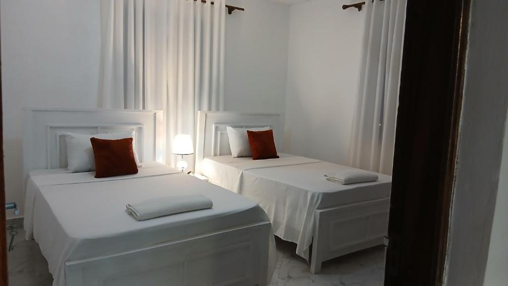 two beds in a white room with white curtains at Hermit Homes in Mombasa