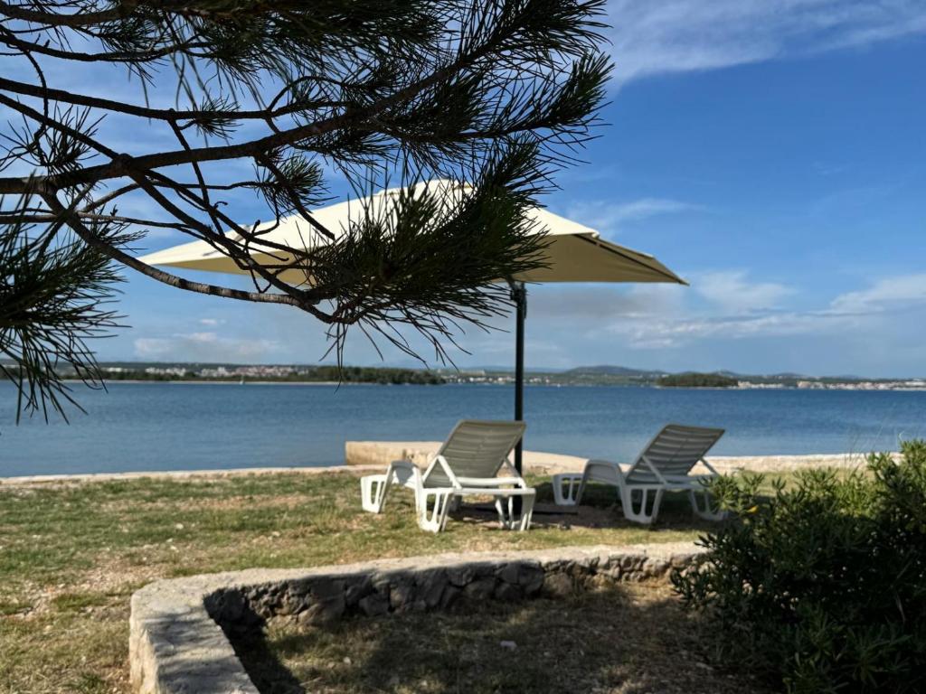 two chairs and an umbrella next to the water at Apartment Lana in Pašman