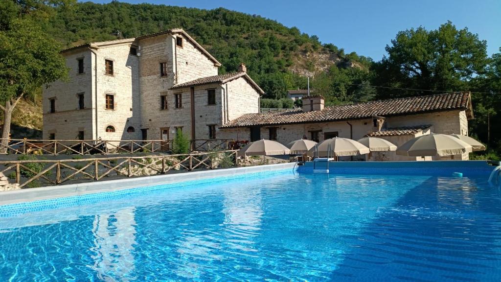 a large swimming pool in front of a building with umbrellas at IL MOLINO del SIGNORE in Pergola