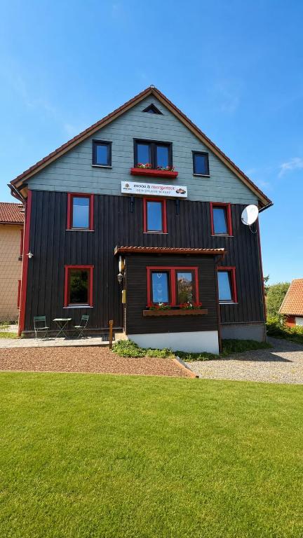 a black house with red windows and a green lawn at Pension moos & morgenrot - St Andreasberg in Sankt Andreasberg