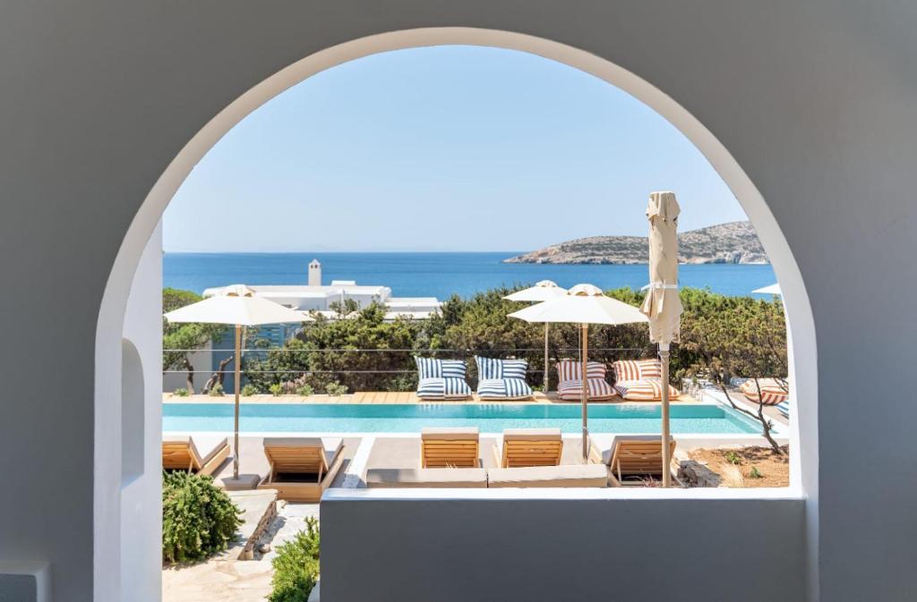 an archway view of a pool with chairs and umbrellas at Oliaros Seaside Lodge in Agios Georgios