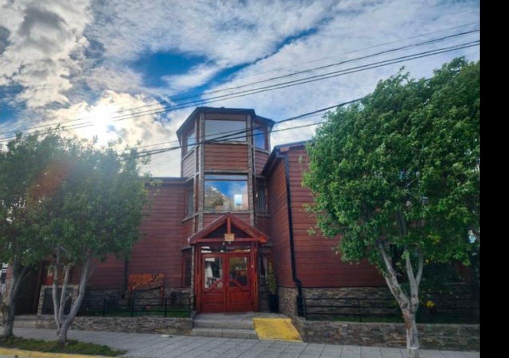 a wooden house with a red door and trees at Hosteria Les Eclaireurs in Ushuaia