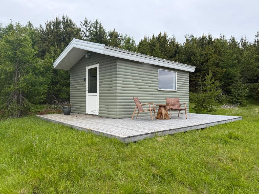 a small green cabin with two chairs and a table at Lífsbót - riverside cottage in Egilsstaðir