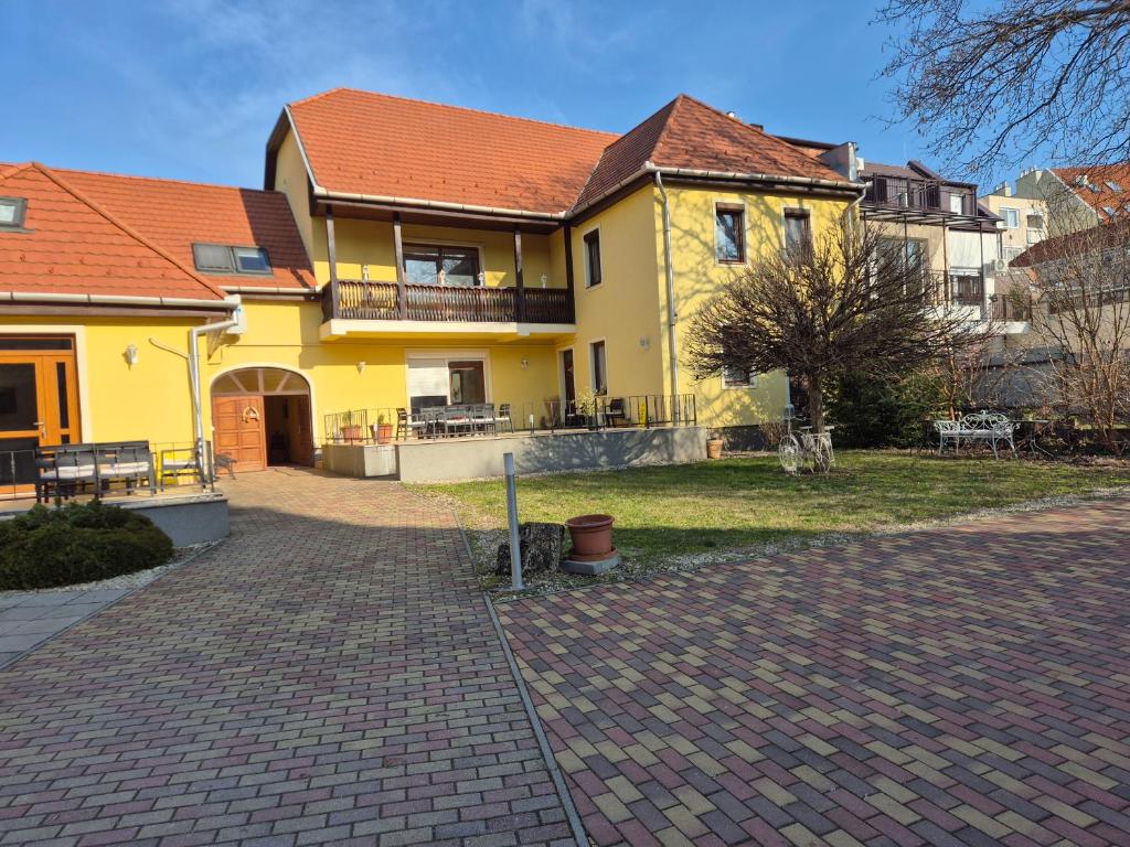 a yellow house with a red roof on a brick driveway at Diófa Vendégház in Eger