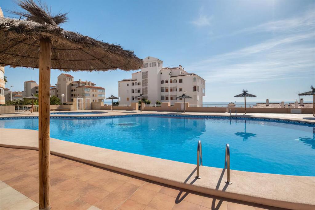 a swimming pool with an umbrella and some buildings at Bungalow Barlovento Playa in Arenales del Sol