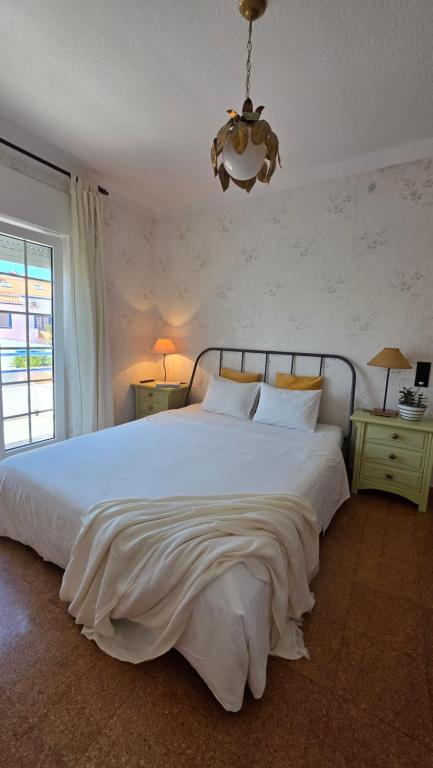 a bedroom with a large white bed and a chandelier at Soleil Bleu in Vila Nova de Milfontes