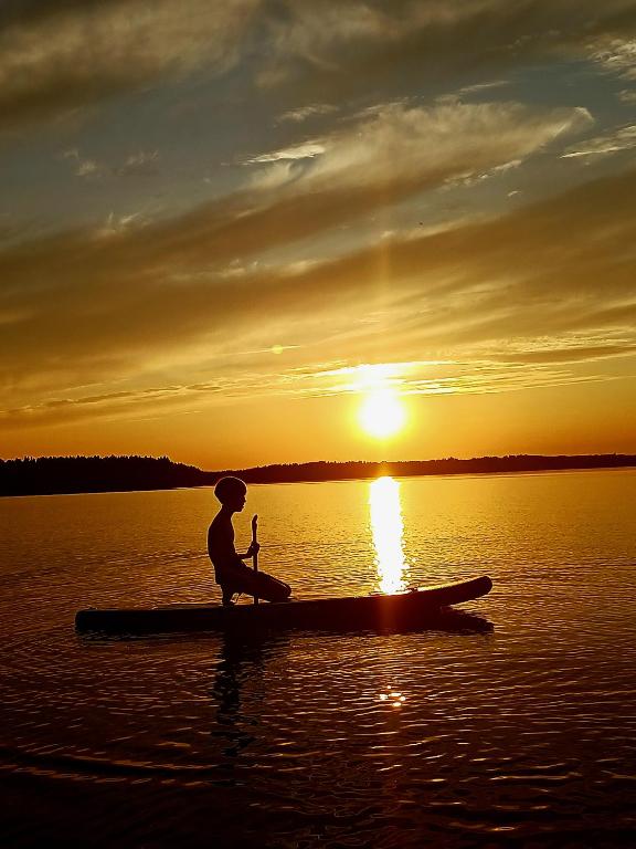 a person sitting on a paddle board in the water at sunset at Loma Kallioniemi in Ähtäri