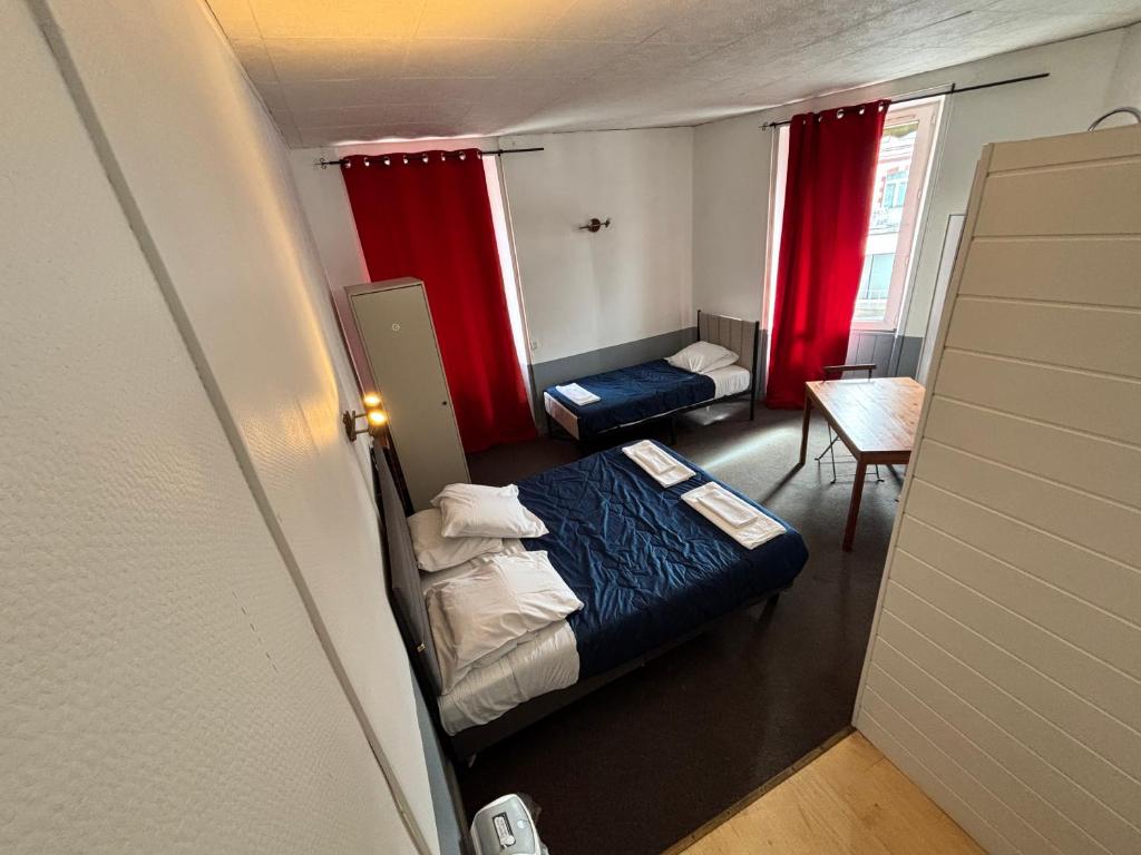 a small room with a bed and a table and red curtains at Le grand cerf Blain in Blain