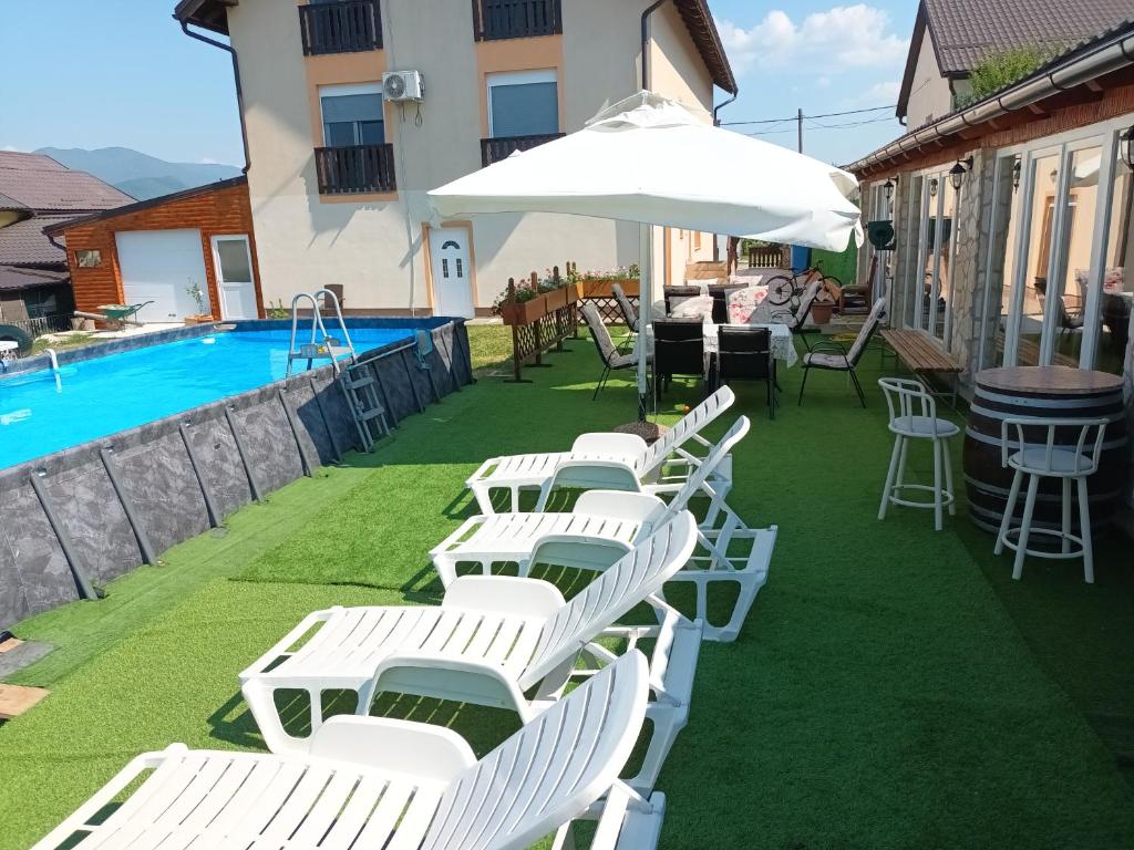 a row of white chairs and an umbrella next to a swimming pool at Guest House Mijić in Korenica