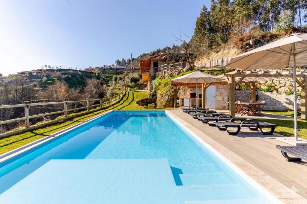 a swimming pool with chairs and umbrellas at Casa do Sol com Piscina and Sauna para 6 Pessoas in Celorico de Basto