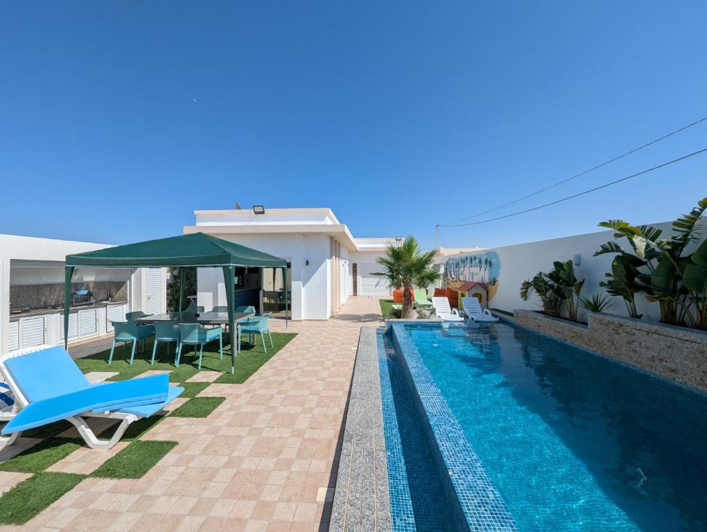 a villa with a swimming pool and blue chairs at Villa SUN SQUARE DJERBA in Awlād ‘Umar
