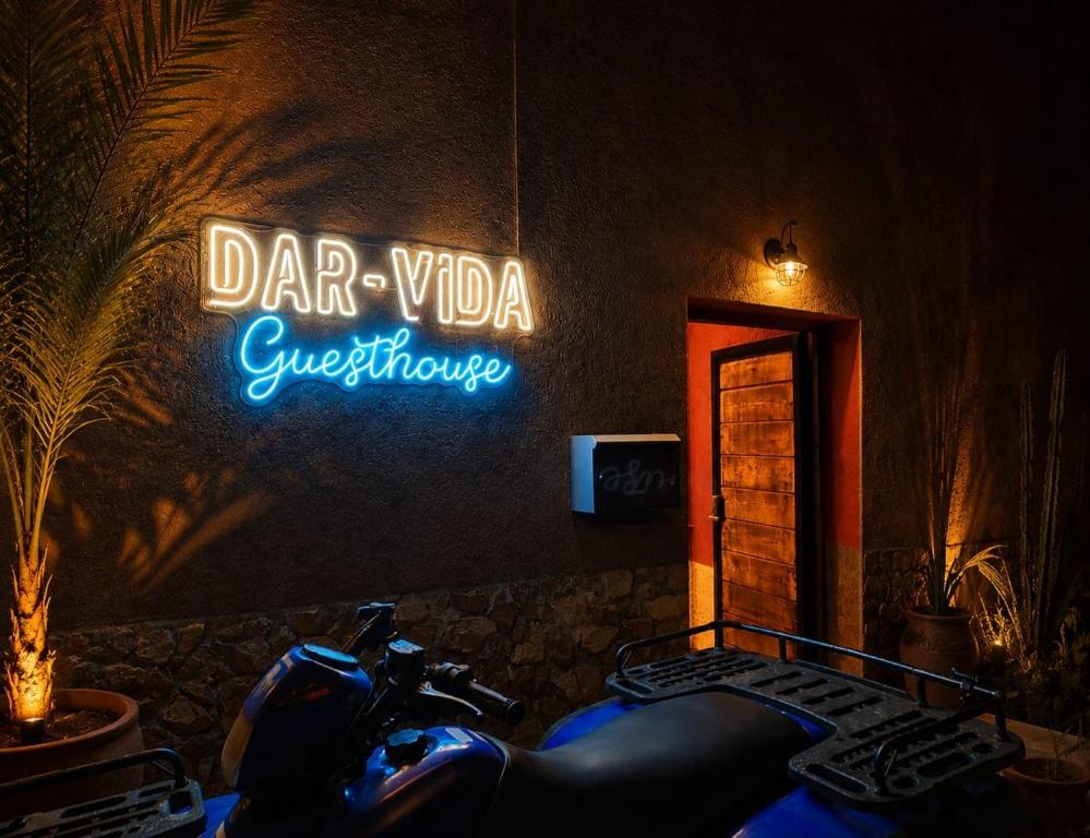 a motorcycle parked in front of a building with a neon sign at DAR-VIDA Guesthouse in Imsouane