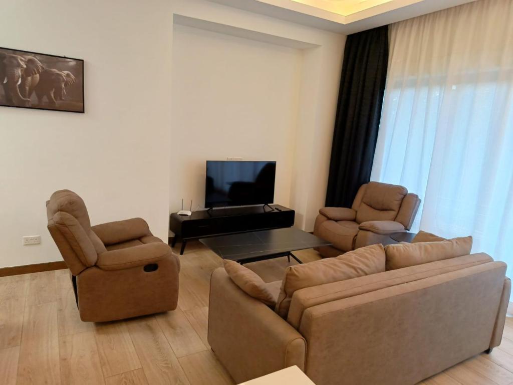 a living room with a couch and two chairs and a television at Intercultural Apartment Nairobi Two Rivers in Nairobi
