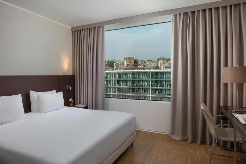 a hotel room with a bed and a large window at NH Savona Darsena in Savona