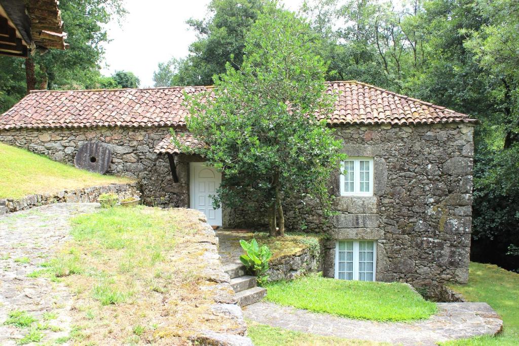 a stone house with a tree in front of it at Casa Moinho da Levada - Refúgio à beira do rio Coura in Paredes de Coura
