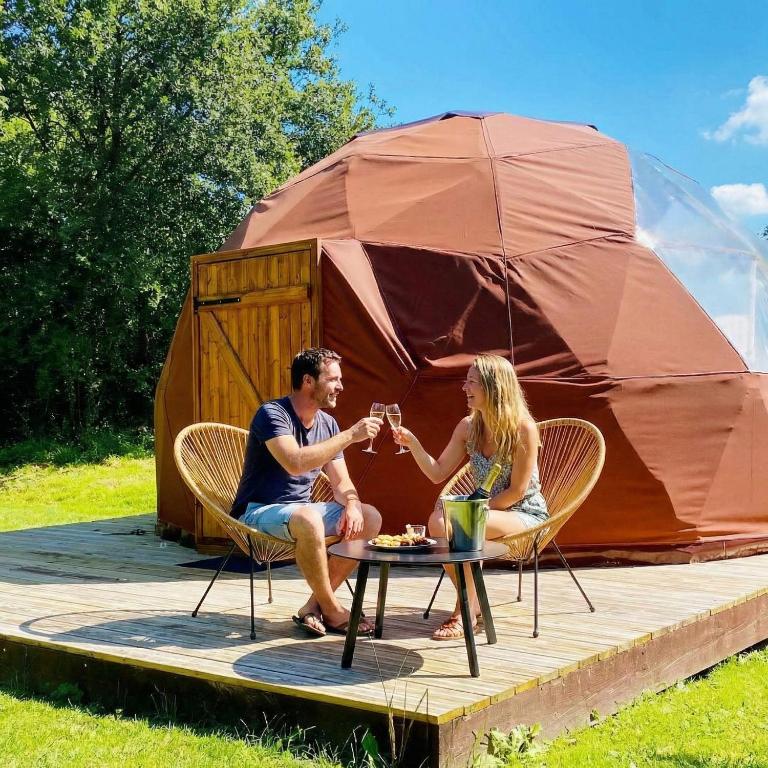 a man and woman drinking wine in front of a tent at Little Wood Lodges in Bailly-aux-Forges