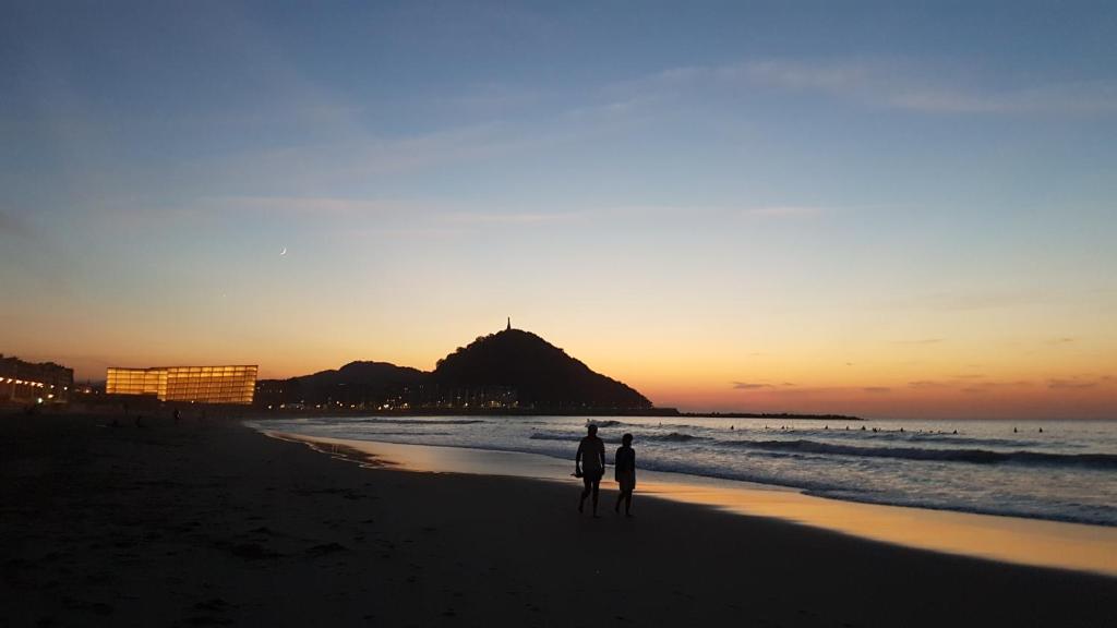 zwei Personen stehen am Strand bei Sonnenuntergang in der Unterkunft Pensión Atxiki in San Sebastián