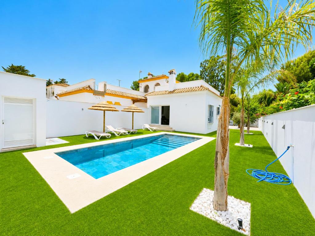a villa with a swimming pool and a palm tree at Playa Fuente del Gallo I in Conil de la Frontera