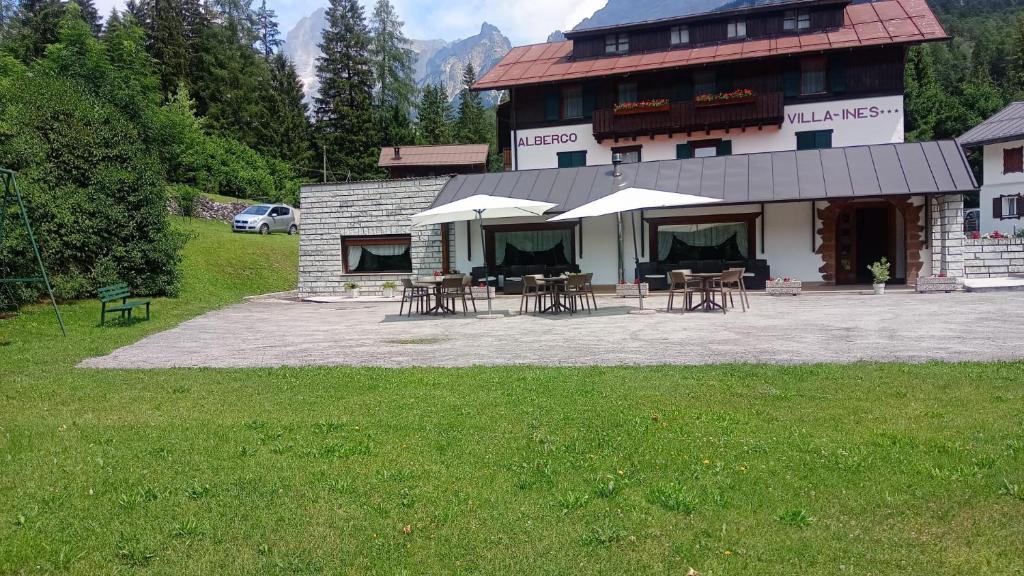 a building with tables and umbrellas in front of it at Hotel Villa Ines in Borca di Cadore