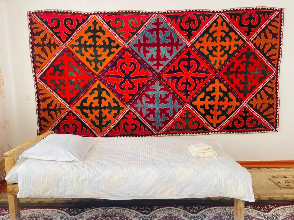 a bed with a red blanket on a wall at Guest house Kyial in Naryn