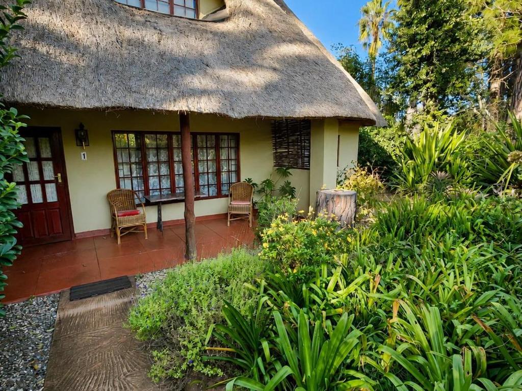 a thatch roofed house with two chairs and a patio at Quiet Mountain Country House in Hekpoort