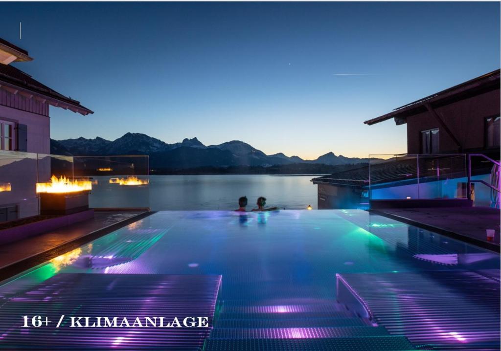a swimming pool with people in the water at night at Hotel am Hopfensee in Füssen