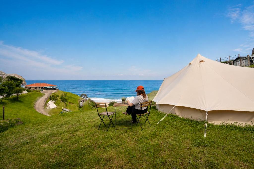 a woman sitting at a table under a tent next to the ocean at Kampaoh Llanes in Vidiago