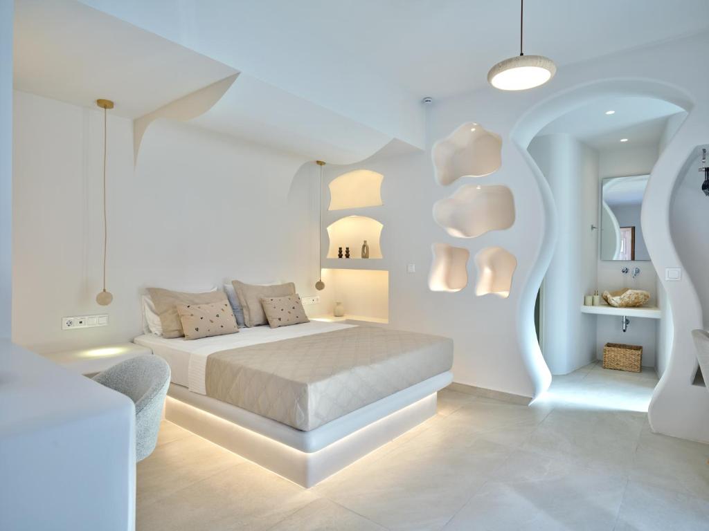 a white bedroom with a bed and a chair at Rocaia Mini Suites Naousa in Naousa