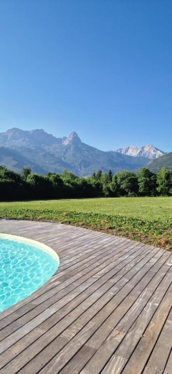 a wooden deck with a pool and mountains in the background at La Maison Bleue - Escale en Ubaye in Saint-Pons