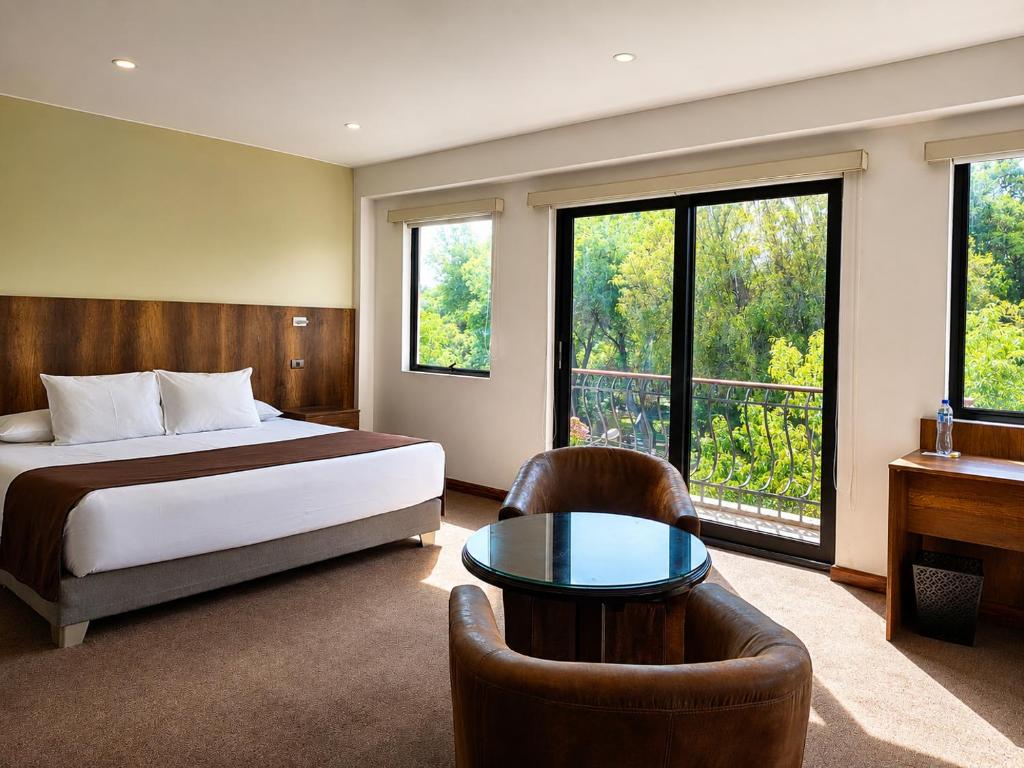 a bedroom with a bed and a table and some windows at Hotel Villa del Carmen in Arequipa