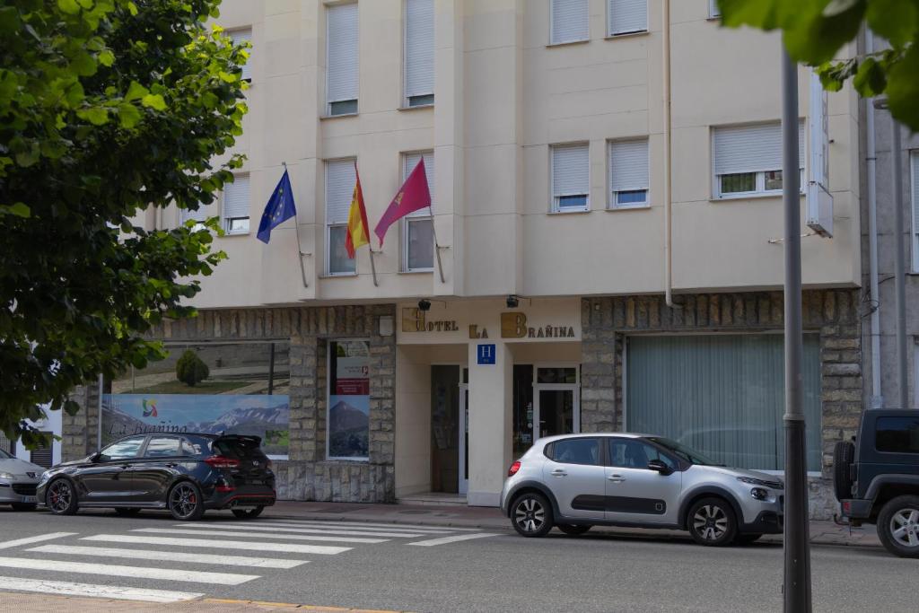 two cars parked in front of a building with flags at Hotel La Brañina in Villablino