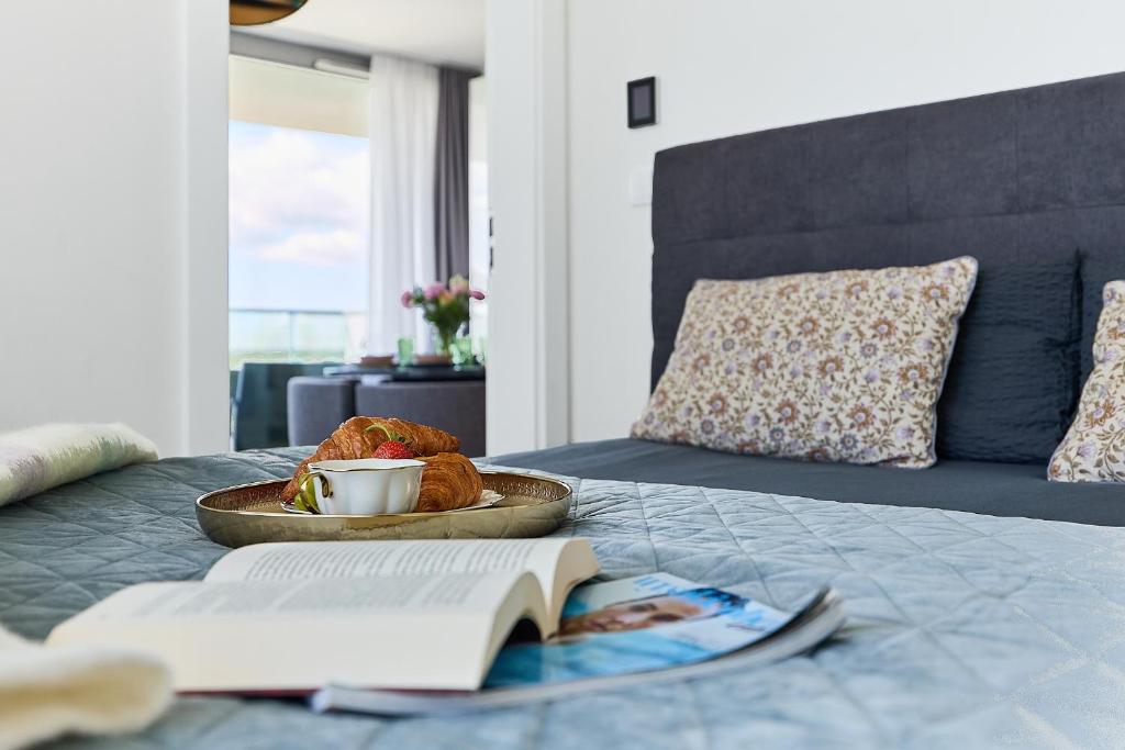 a plate of food and a book on a bed at WAVE Seaview in Międzyzdroje