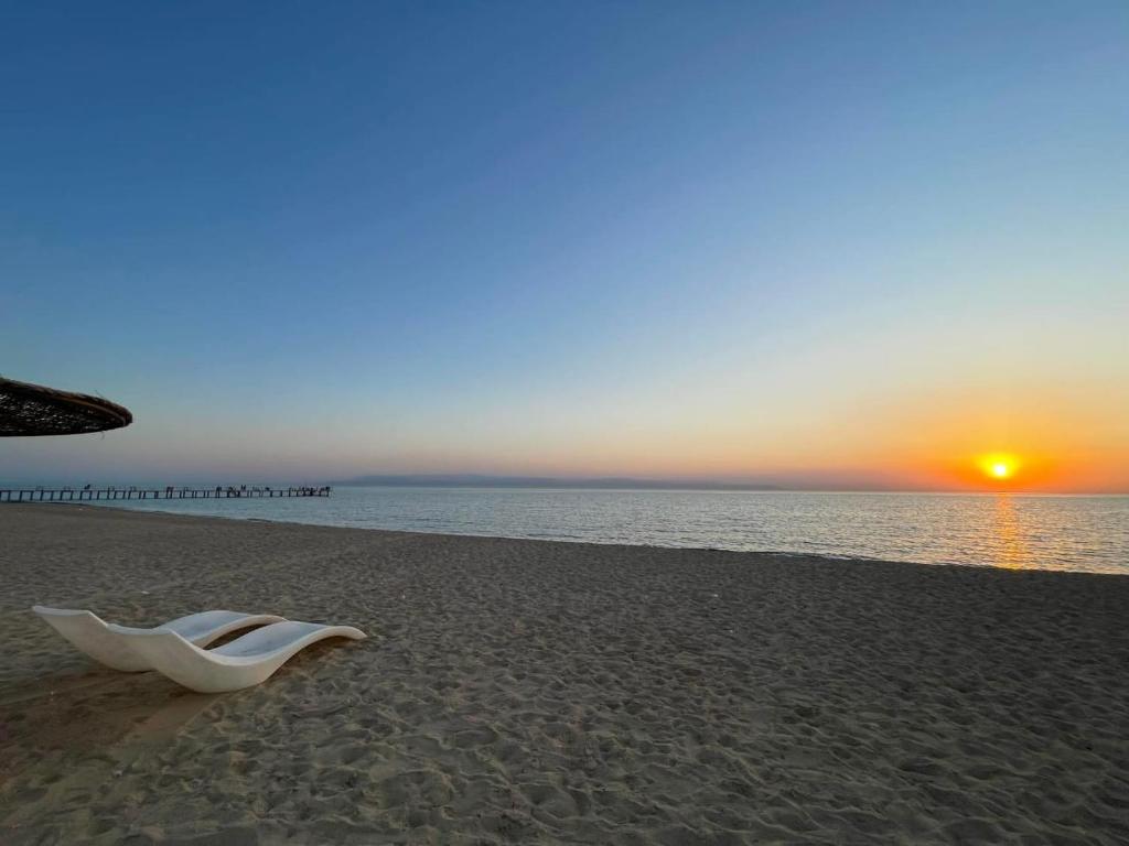 a white chair sitting on a beach with the sunset at White Bay Ras Sedr وايت باي راس سدر in Ras Sedr